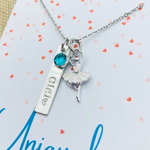 May include: A silver necklace with a silver charm that says "Gigi" and a ballerina charm. The ballerina charm is pink and white and has a blue gemstone on the necklace chain.