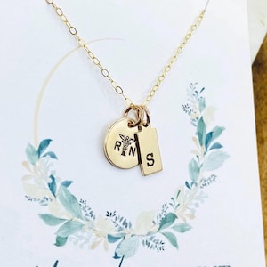 May include: Gold necklace with three charms: a round charm with the letters "RN" and a medical symbol, a smaller round charm with the letter "S", and a rectangular charm with the letter "S".