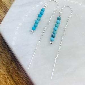 May include: A pair of silver chain earrings with turquoise beads. The earrings are long and dangle from the earlobe.