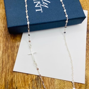 May include: A silver chain necklace with a small silver cross pendant. The chain is made of small, oval-shaped links.