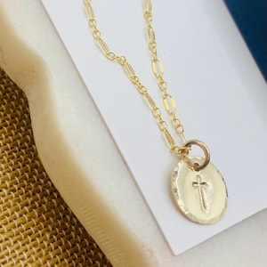 May include: A gold chain necklace with a small, oval-shaped pendant featuring a cross design.