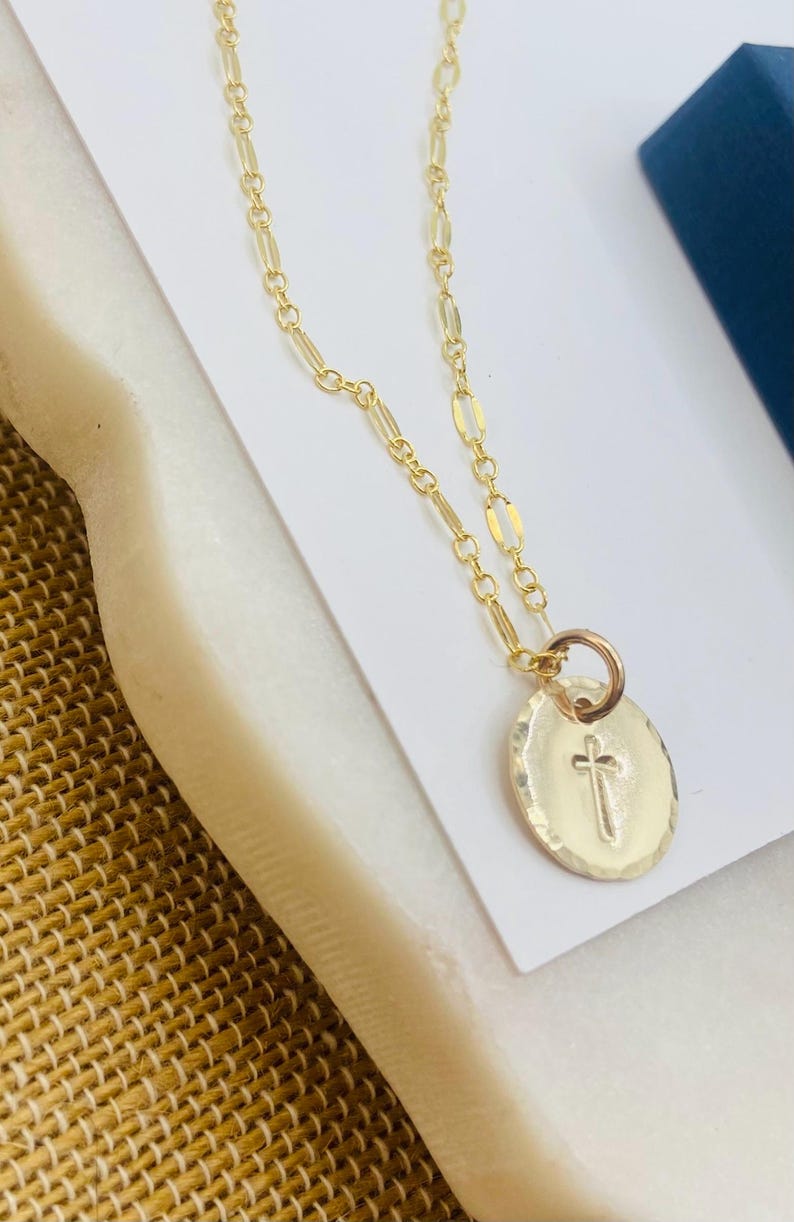 May include: A gold chain necklace with a small, oval-shaped pendant featuring a cross design.