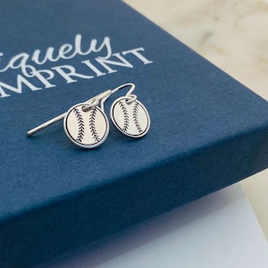 May include: A pair of silver earrings with a baseball design. The earrings are on a blue background with the text "uniquely IMPRINT" visible.
