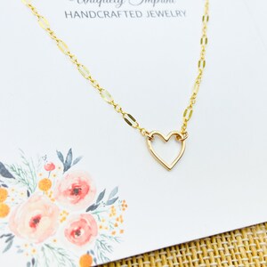 May include: A gold necklace with a delicate open heart pendant. The necklace is on a white card with the text "Uniquely Imprint HANDCRAFTED JEWELRY".