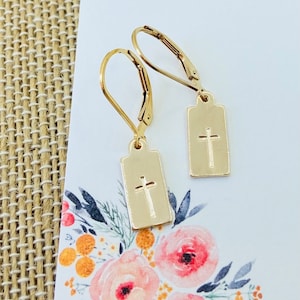 May include: A pair of gold-toned dangle earrings with a small rectangular charm featuring a cross design.