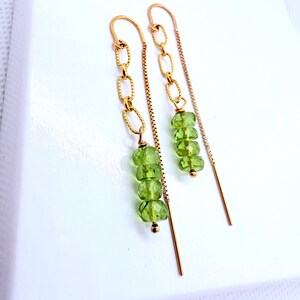 May include: A pair of gold-tone threader earrings featuring a delicate box chain design. Each earring is accented with a short vertical chain segment and a cluster of four small, faceted, translucent light green peridot-colored beads.