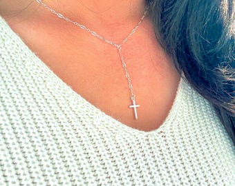 May include: A silver-colored Y-shaped necklace with a small cross pendant. The necklace is delicate and hangs from a chain with an oval link design. The cross is centered and hangs at the end of the Y-shaped drop.