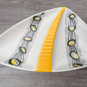 Può includere: Un piatto da portata triangolare in ceramica bianca con una striscia centrale gialla in rilievo e due bande decorative simmetriche di pennellate grigie con cerchi neri disegnati a mano contenenti accenti gialli su entrambi i lati.