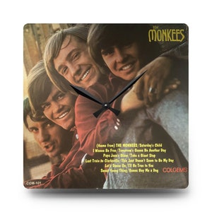 May include: A square clock with a black face and hands. The clock face is a vintage record album cover featuring a photo of the band The Monkees. The album cover has the band's name and the title of the album, "The Monkees", printed in gold letters. The album cover also lists the songs on the album, including "Saturday's Child", "I Wanna Be Free", "Tomorrow's Gonna Be Another Day", "Papa Jean's Blues", "Take a Giant Step", "Last Train to Clarksville", "This Just Doesn't Seem to Be My Day", "Let's Dance On", "I'll Be True to You", "Sweet Young Thing", and "Gonna Buy Me a Dog". The album cover also has the record label, "Colgems", printed in the bottom right corner.