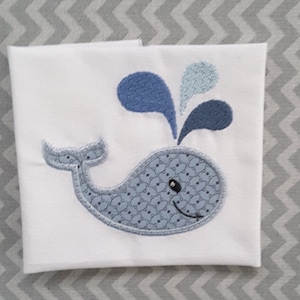 May include: A white cloth burp cloth with a blue whale and water spout embroidered on it.