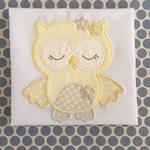 Può includere: Un gufo giallo ricamato con gli occhi chiusi e un fiore sulla testa. Il gufo ha un motivo a pois sulle ali e sul corpo.