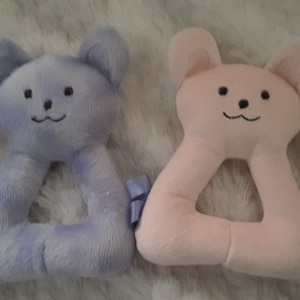 May include: Two plush teddy bear shaped baby teethers. One is light blue and the other is pink.