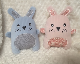 May include: Two plush bunny toys, one blue and one pink, with embroidered faces and floral patterns.