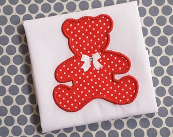 May include: A white fabric with a red and white polka dot teddy bear applique. The teddy bear has a white bow with a rhinestone in the center.