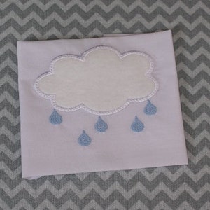 May include: A white cloud with blue raindrops embroidered on a white fabric. The fabric has a grey chevron pattern.