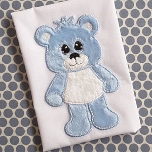 Może przedstawiać: Pluszowy miś w kolorze niebieskim, wyszyty z białym futerkiem na klatce piersiowej i brzuchu. Miś ma duże czarne oczy i uszyty uśmiech.