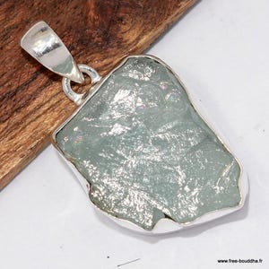 May include: A silver pendant with a large, irregularly shaped, pale blue-green gemstone. The stone is set in a silver bezel with a loop for a chain. The pendant is displayed on a wooden surface.