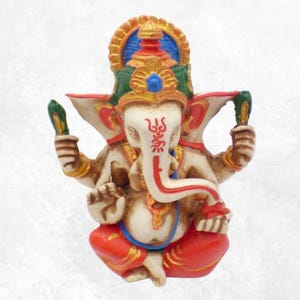 Peut inclure: Figurine détaillée de la divinité hindoue Ganesha, assise avec plusieurs bras. La statue présente une tête d'éléphant blanche, des accents rouges et dorés, et est ornée d'une coiffe verte et bleue. La figurine est assise sur une base rouge.