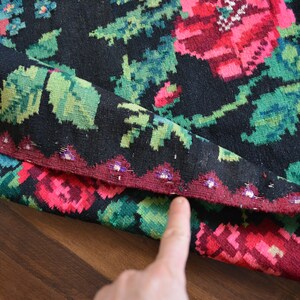 May include: Close-up of a black and red woven rug with floral patterns. The rug has a fringe border and is folded in half.