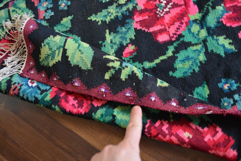 May include: Close-up of a black and red woven rug with floral patterns. The rug has a fringe border and is folded in half.
