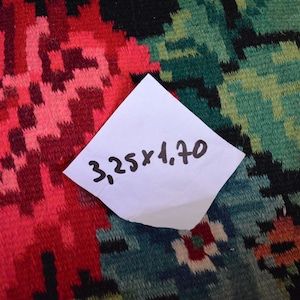 May include: A close-up of a red, green, and black patterned fabric with a white note on top. The note says "3.25 x 4.70".