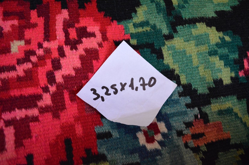 May include: A close-up of a red, green, and black patterned fabric with a white note on top. The note says "3.25 x 4.70".