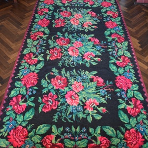 May include: A black rug with a floral pattern featuring red, pink, and green flowers. The rug has a fringe border.
