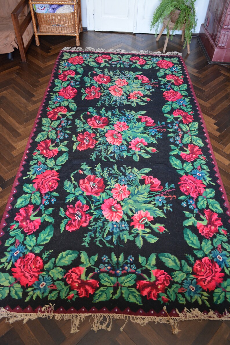 May include: A black rug with a floral pattern featuring red, pink, and green flowers. The rug has a fringe border.
