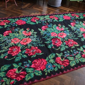 May include: A black rug with a floral pattern featuring red, pink, and green flowers. The rug has a fringe border.