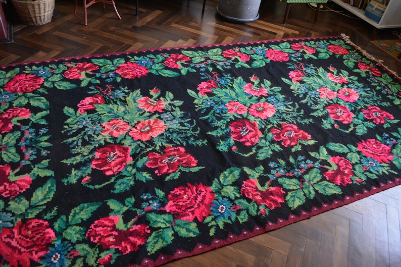 May include: A black rug with a floral pattern featuring red, pink, and green flowers. The rug has a fringe border.