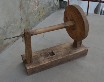 Könnte beinhalten: Ein hölzernes Spinnrad mit einem großen runden Holzrad und einem langen Holzgriff. Das Rad ist auf einem Holzsockel montiert.