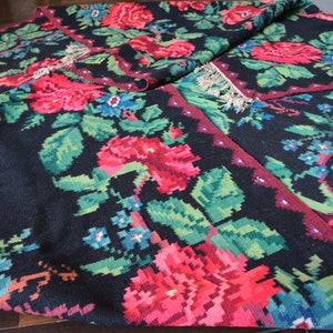 May include: A black rug with a floral pattern featuring red, green, and blue flowers. The rug has a fringed edge and is woven with a traditional design.