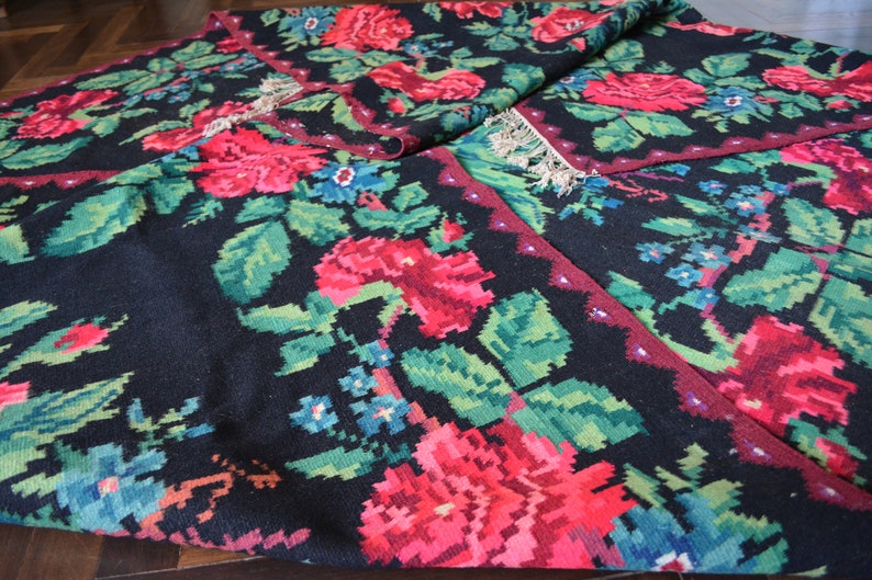May include: A black rug with a floral pattern featuring red, green, and blue flowers. The rug has a fringed edge and is woven with a traditional design.