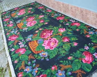 May include: A black wool rug with a floral pattern featuring pink, red, green, and blue flowers. The rug has a woven texture and is decorated with baskets of flowers.