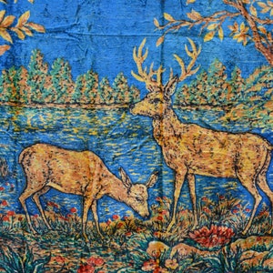 May include: A tapestry depicting two deer in a forest scene. The deer are golden brown with antlers, set against a blue and green backdrop of trees, water, and foliage. The artwork has a vintage, textured appearance.