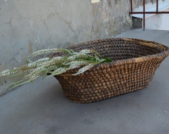 May include: A large, oval-shaped wicker basket with a brown, woven pattern. The basket is filled with white flowers.