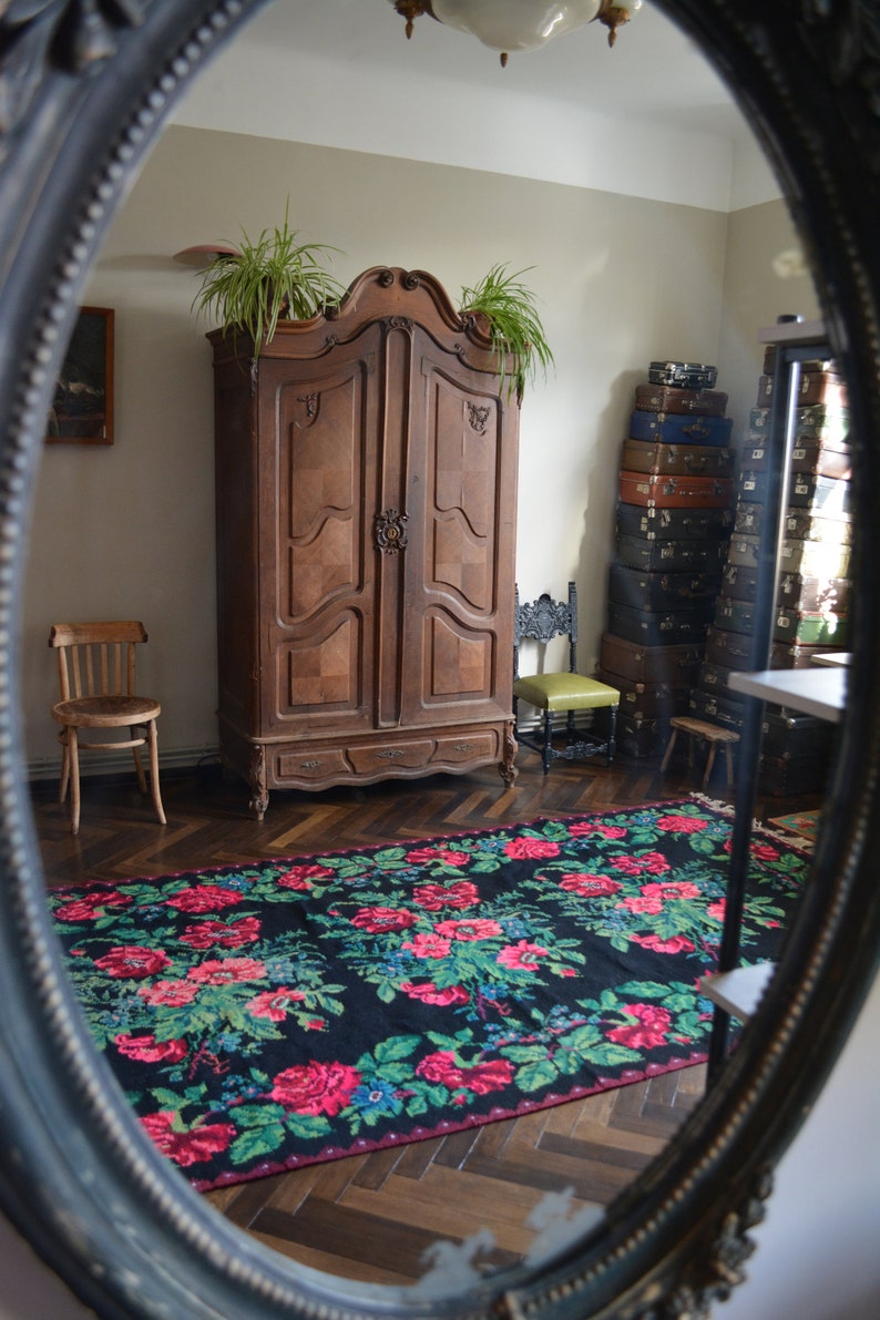 May include: A vintage wooden armoire with two doors and a drawer, standing in a room with a patterned rug and a stack of suitcases. The armoire has ornate carvings and a dark wood finish.