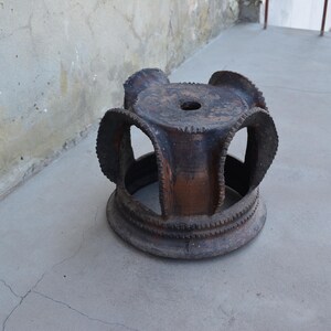 May include: A dark brown ceramic stool with a circular top and a unique, openwork design. The stool has a rustic, aged appearance.