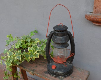 May include: A black oil lamp with a red handle and a glass globe sits on a wooden table with a green and yellow ivy plant.
