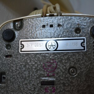 Puede incluir: Primer plano de la parte inferior de un tel&eacute;fono rotatorio beige con una etiqueta plateada que dice "3 FP 120 57" y "II 1969". La etiqueta tambi&eacute;n presenta un logotipo con la palabra "Telefunken".