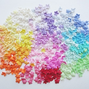 Puede incluir: Surtido de pequeñas flores de papel en un arcoíris de colores, incluyendo blanco, amarillo, naranja, rosa, rojo, azul claro, azul oscuro y verde. Las flores están dispuestas en círculo sobre un fondo blanco.