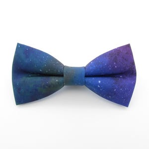 Puede incluir: Una pajarita azul y morada con estampado de galaxia.