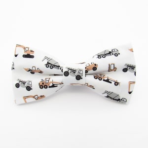 May include: White bow tie with a pattern of construction vehicles in shades of brown, gray, and black.