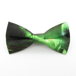 Puede incluir: Una pajarita con un vibrante diseño espacial verde y negro. La tela presenta un patrón de nebulosa arremolinada con toques de blanco y verde, creando una estética cósmica. Un accesorio clásico.