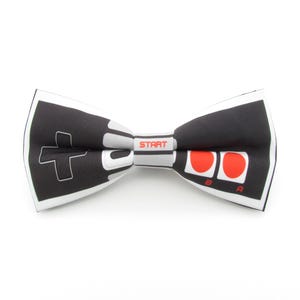 Könnte beinhalten: Ein schwarz-weißes Fliege mit einem roten und weißen Videospiel-Controller-Design. Der Controller hat die Wörter "START", "A" und "B" aufgedruckt.