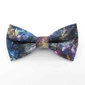 Puede incluir: Una pajarita azul oscuro con un estampado floral colorido. El estampado presenta una variedad de flores en tonos de rosa, morado y azul, con detalles dorados. La pajarita está hecha de una tela suave y cómoda.
