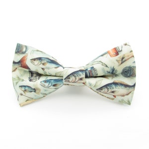 May include: A light green bow tie featuring a pattern of fish and fishing equipment. The bow tie is made from fabric and has a subtle sheen.