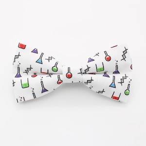 May include: White bow tie with a repeating pattern of colourful laboratory flasks and beakers in red, green, purple, and blue. The bow tie also has a black and white DNA strand design.