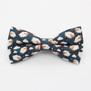 May include: A dark blue bow tie featuring a white sheep and cloud pattern. The sheep are brown and white and have a cartoonish appearance.