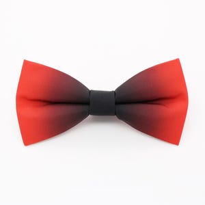 May include: A pre-tied bow tie featuring a smooth fabric with a colour gradient that transitions from a vibrant red at the outer edges to a deep black at the centre knot. The bow tie has a classic butterfly shape with crisp, clean edges.